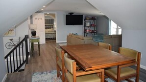 Un comedor con una mesa y sillas de madera, una escalera, un sofá y un televisor en la pared.