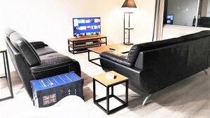 A modern living room with a black leather sofa, a wooden coffee table, and a television displaying a video call. - Le Greyhound - Grand Appartement Centre-ville (Soissons)