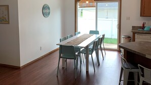 Ein Essbereich mit einem Holztisch und Stühlen, einer Hängelampe und Blick ins Freie durch eine Glastür.