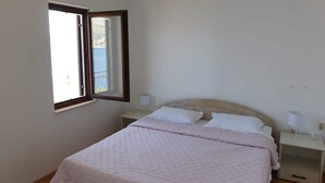 Un dormitorio con cama, mesita de noche, lámpara y ventana.