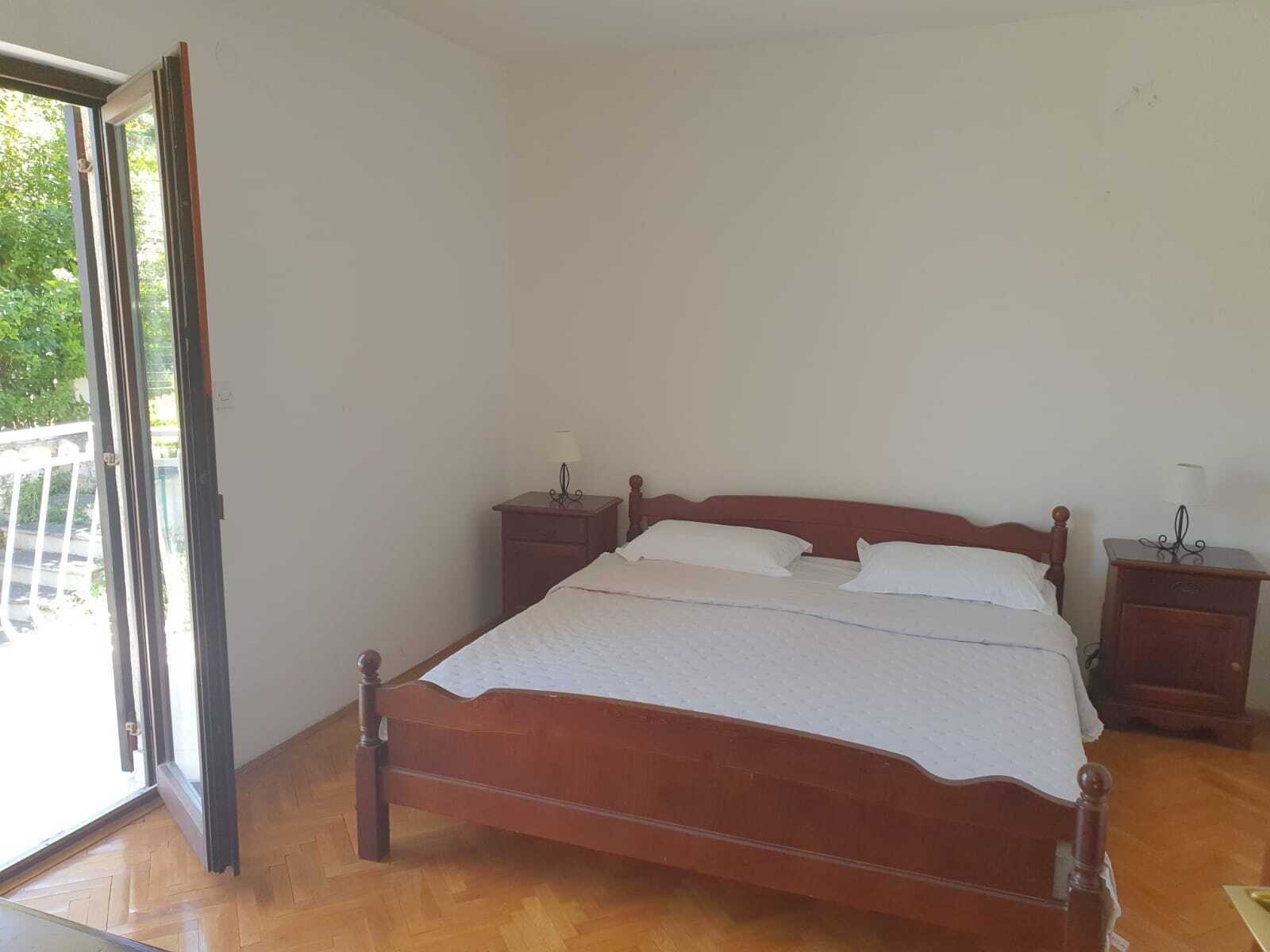 A bedroom with a wooden bed, two bedside tables, and a sliding glass door leading to a balcony.