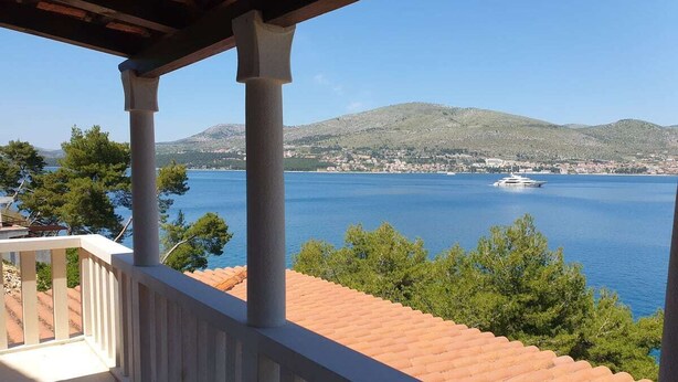 Un balcón con vista a un mar tranquilo y colinas lejanas.