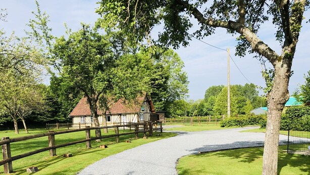 A gravel path leading to a traditional building with a sloped roof, surrounded by a wooden fence and lush greenery.