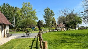 A well-maintained grassy area with a wooden fence, a gravel path, and a building with a tiled roof.