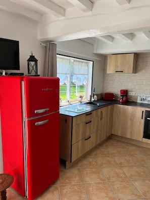 A kitchen with a red refrigerator, wooden cabinets, a black countertop, and a window with a view of greenery.