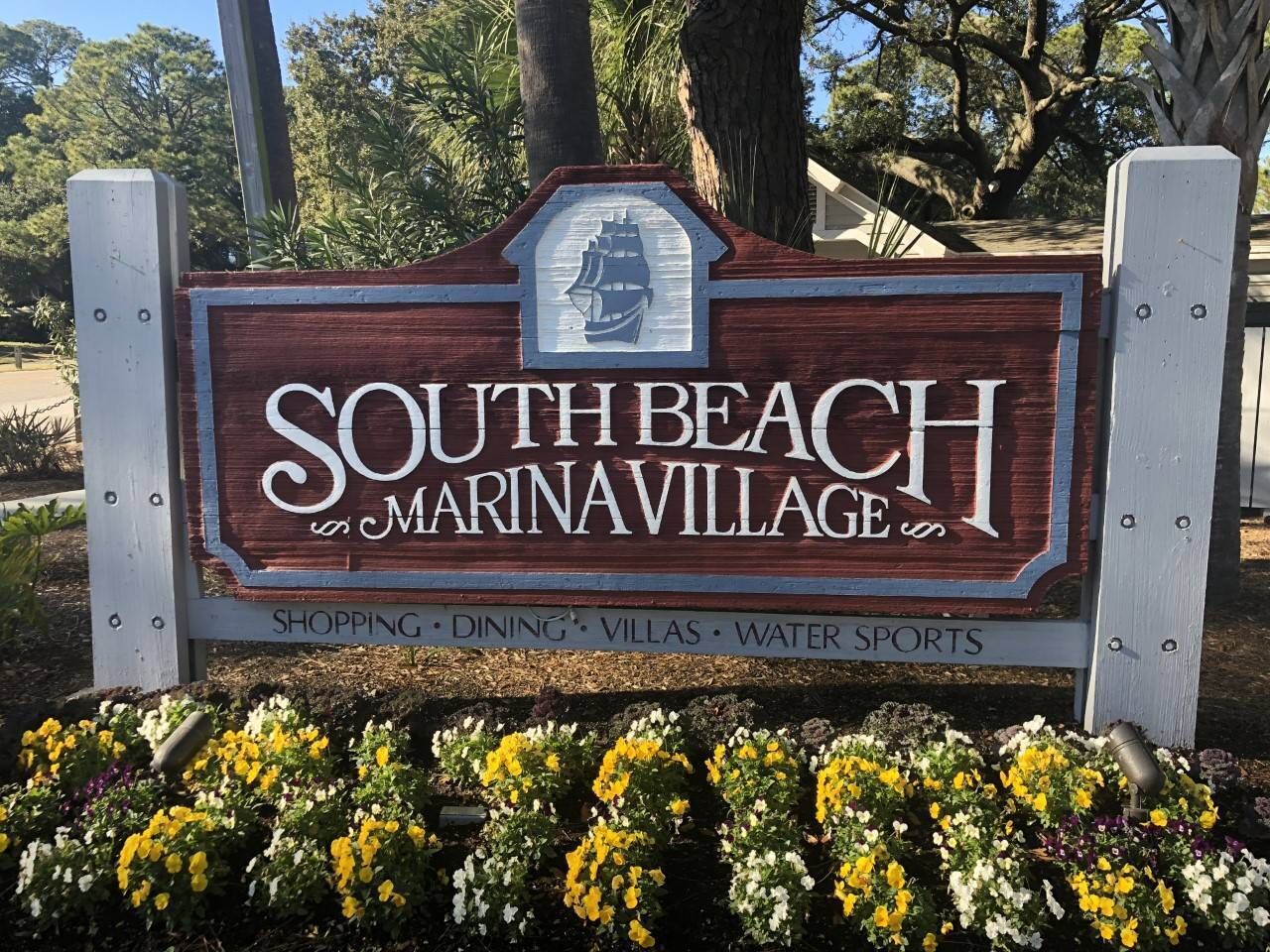 Een houten bordje voor South Beach Marinavillage, met een schip-embleem, waarop voorzieningen staan vermeld zoals winkels, restaurants, villa's en watersport.