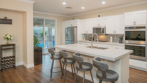 A modern kitchen with white cabinetry, stainless steel appliances, and a large island with bar stools. - Good Vibes off the strip, 5BR, Secret room, 2 King Beds, Pool and Spa (Henderson)
