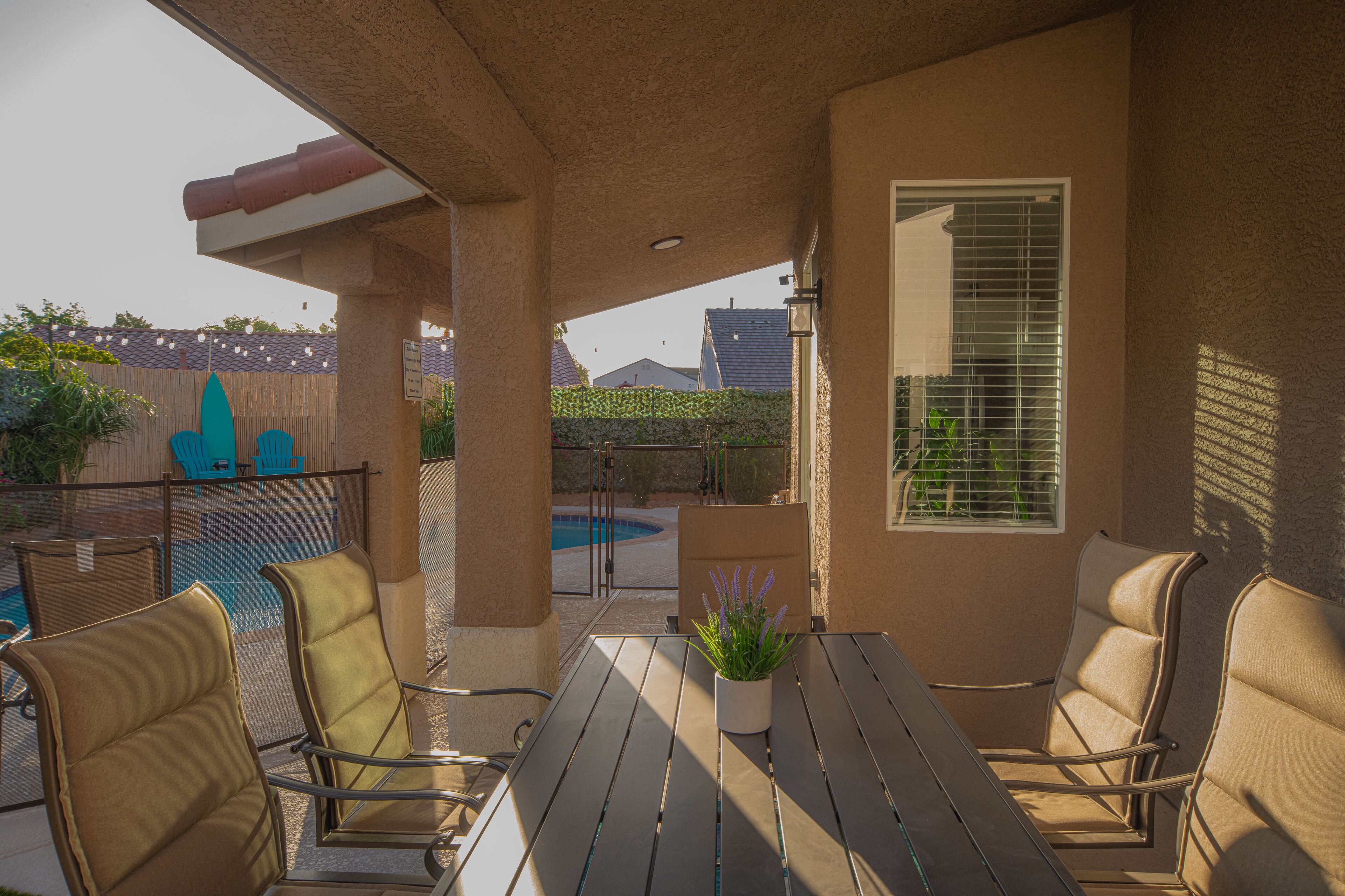 A covered outdoor seating area with a pool, chairs, and a table.