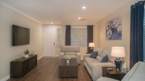A living room with a flat-screen TV, a sofa, a coffee table, and a lamp. - Good Vibes off the strip, 5BR, Secret room, 2 King Beds, Pool and Spa (Henderson)