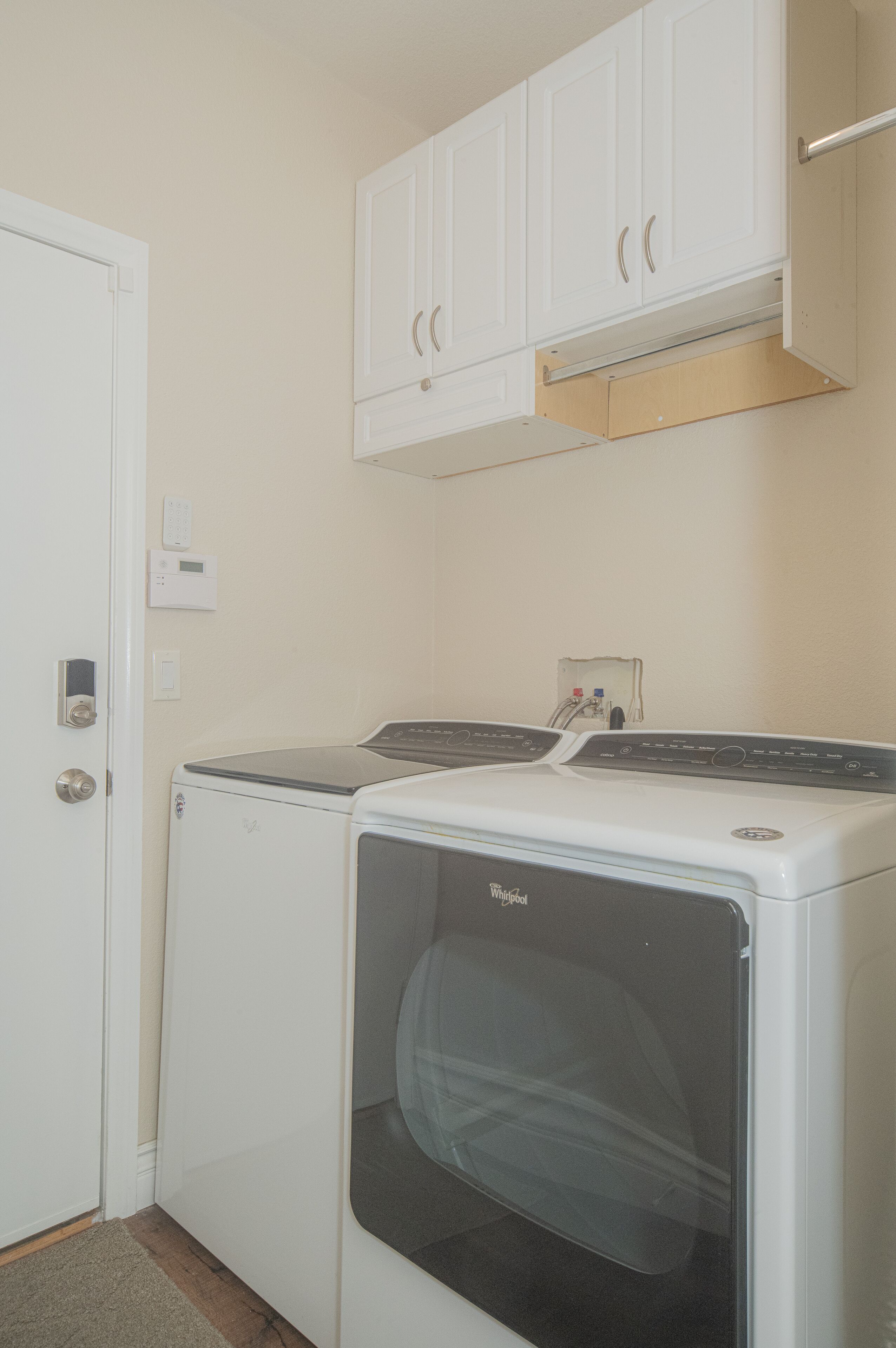 Une buanderie équipée de deux machines à laver et deux sèche-linge blancs, une porte blanche et un meuble blanc placé au-dessus des sèche-linge.
