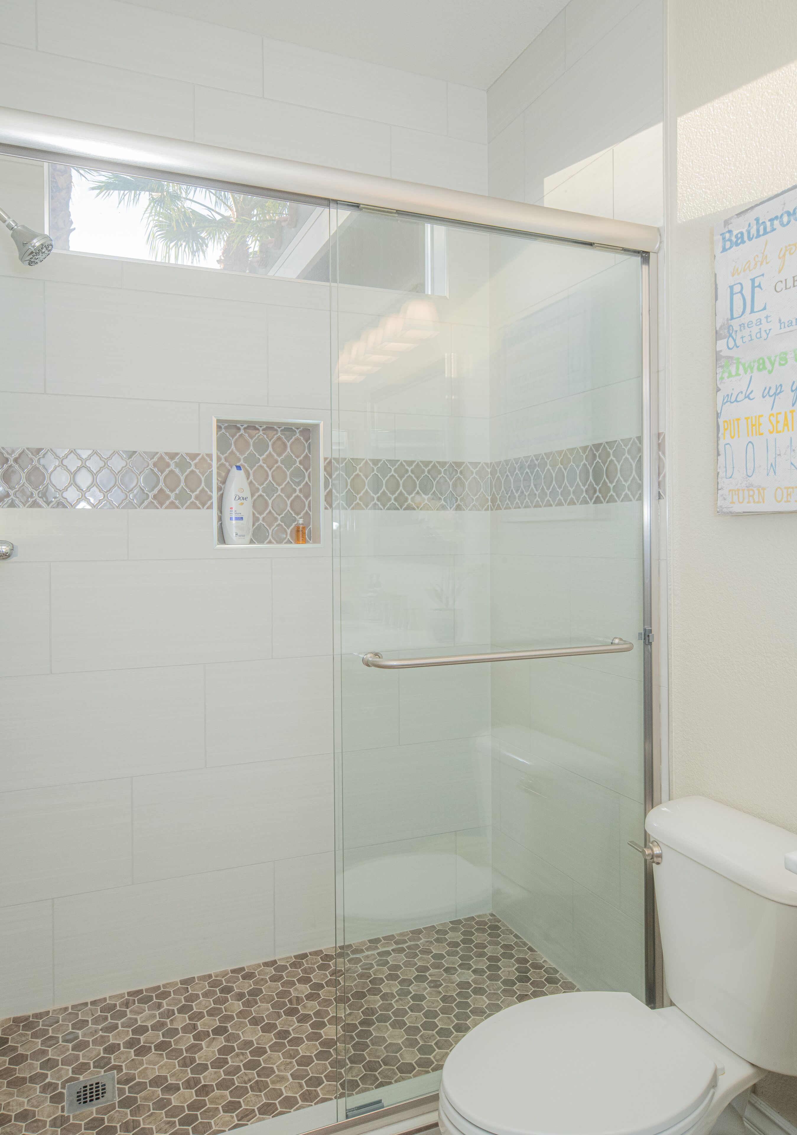 A bathroom with a glass shower enclosure, a toilet, and a tiled floor.