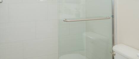 A bathroom with a glass shower enclosure, a toilet, and a tiled floor.