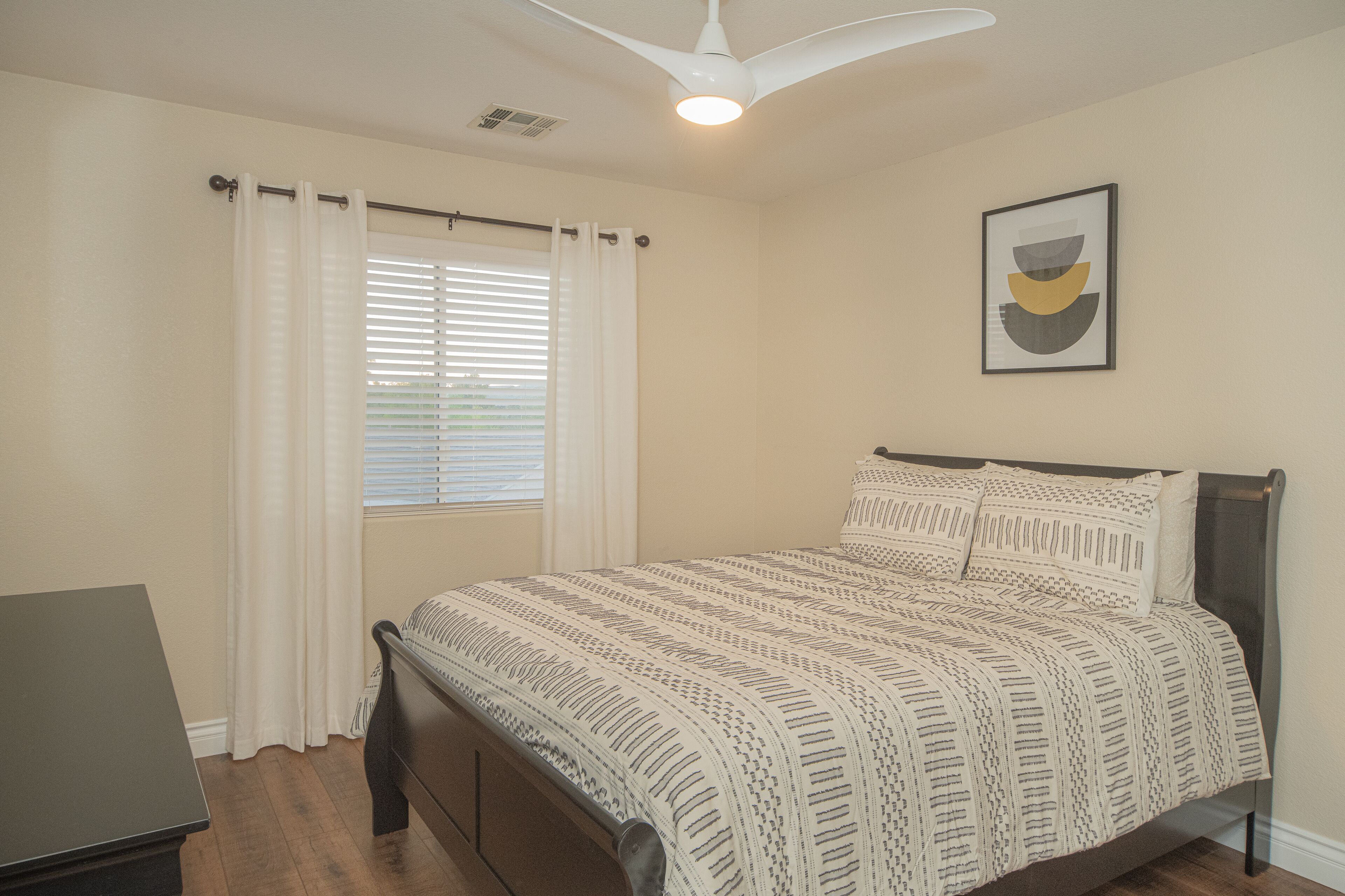 A bedroom with a bed, a desk, and a ceiling fan.