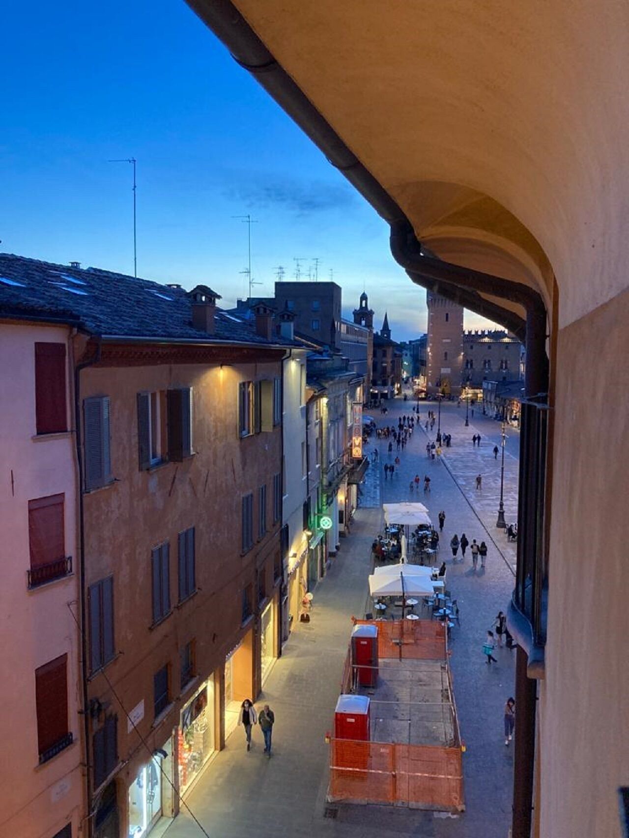 Una vista di una strada con edifici, cielo sereno e alcune persone che camminano.