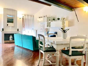 A cozy living room with a teal sofa, white dining table, and matching chairs. - Maison Contrari (Ferrara)
