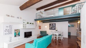 Una sala de estar moderna con un sofá color turquesa, mueble blanco para la televisión y un comedor con sillas y mesa blancos.