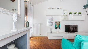 Una sala de estar moderna con una chimenea blanca, un televisor y un sofá color turquesa.