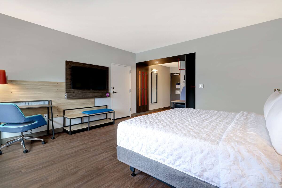 A hotel room with a bed, a desk, a chair, and a TV.