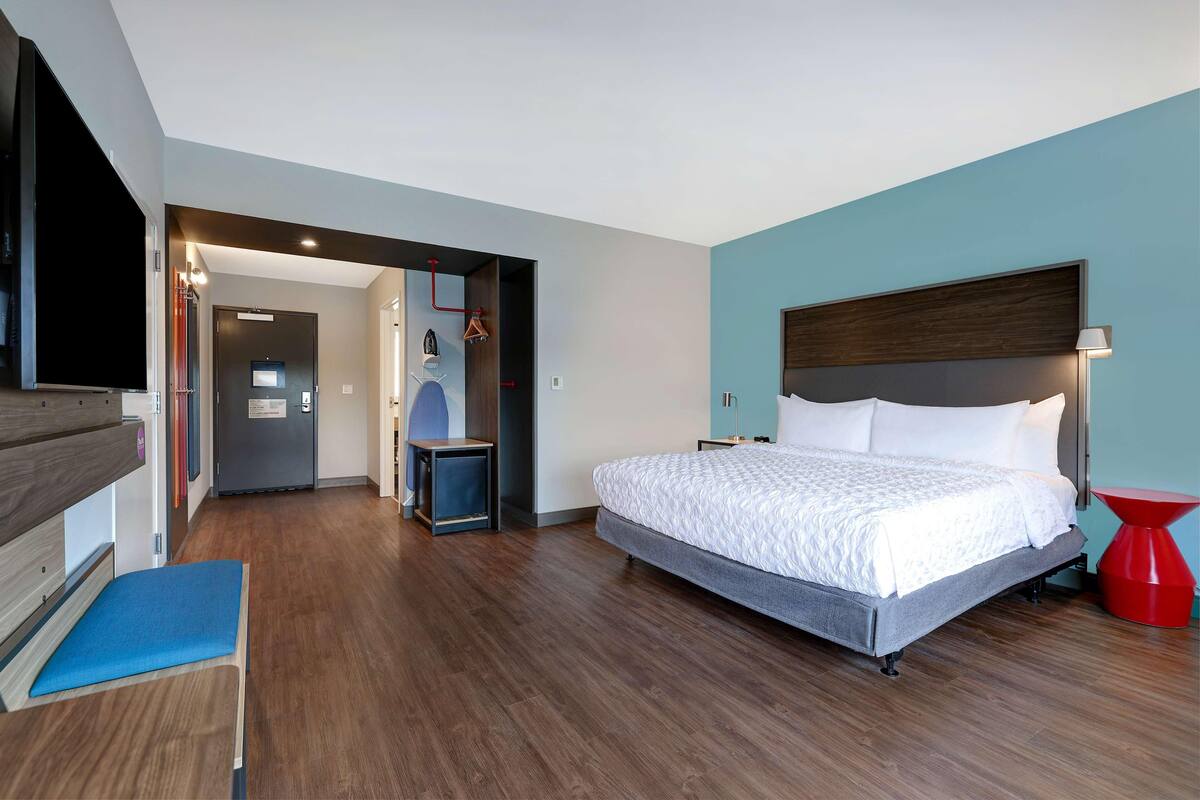 A modern hotel room with a large bed, a TV, a desk, and a red accent chair.