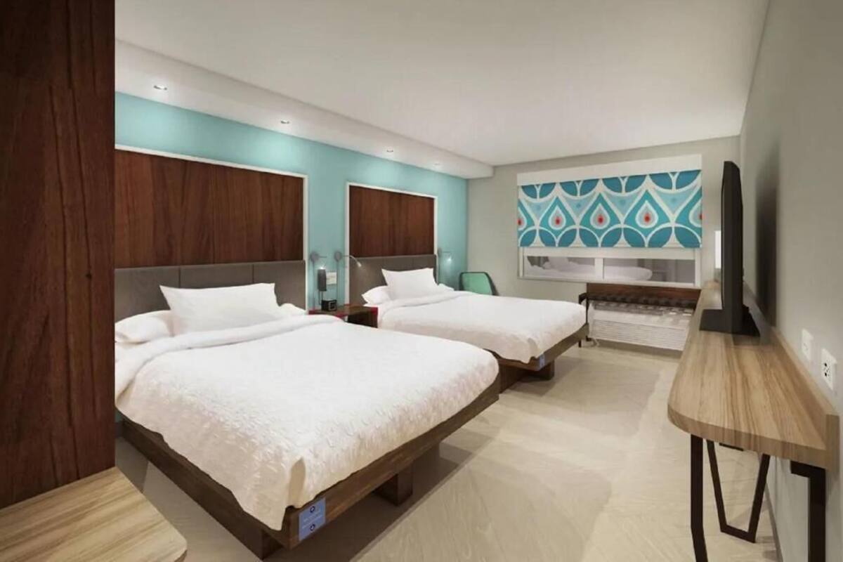 A modern hotel room with two beds, a wooden desk, and a TV.