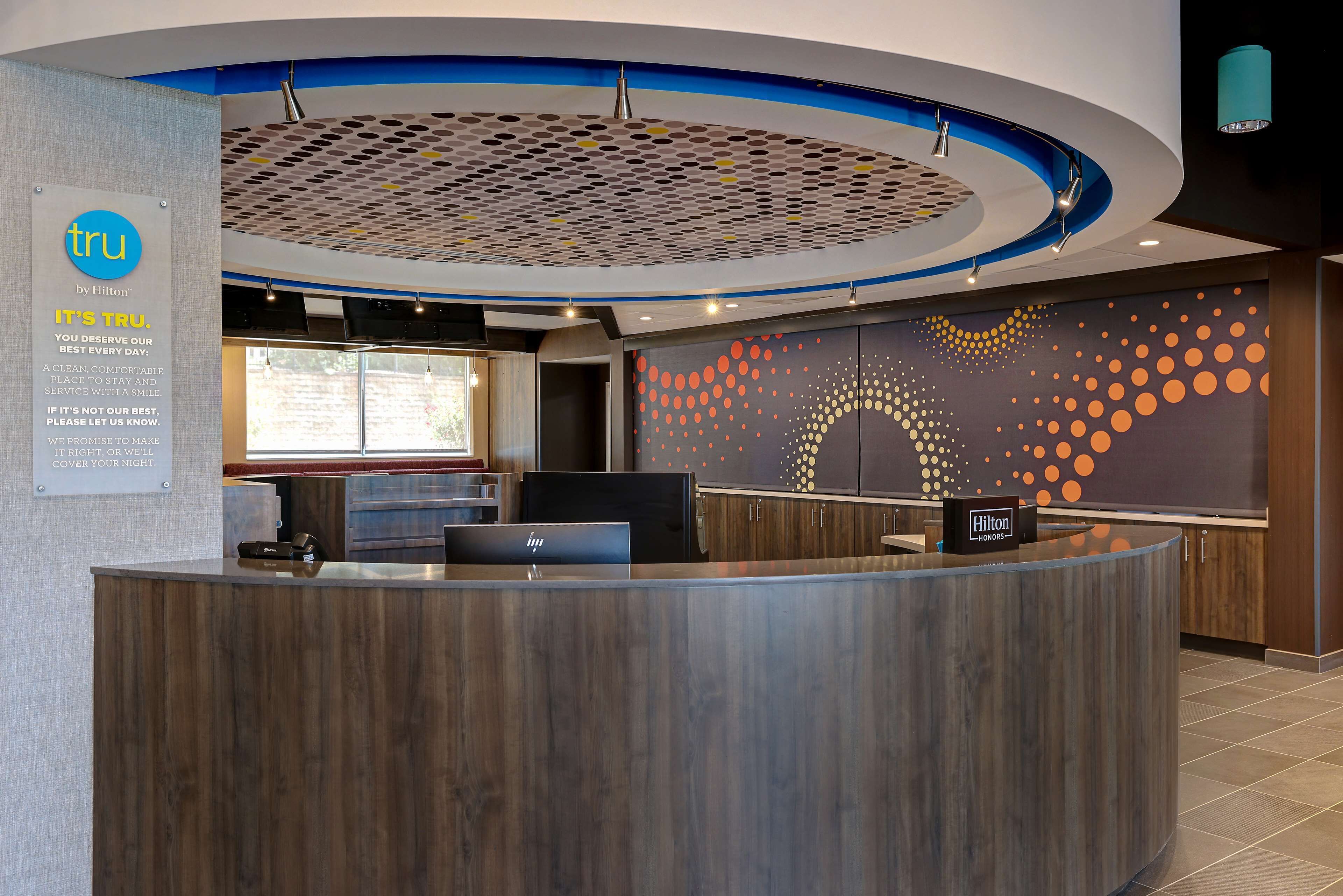 A modern hotel reception area with a wooden reception desk, a digital display, and a wall with a dot pattern design.