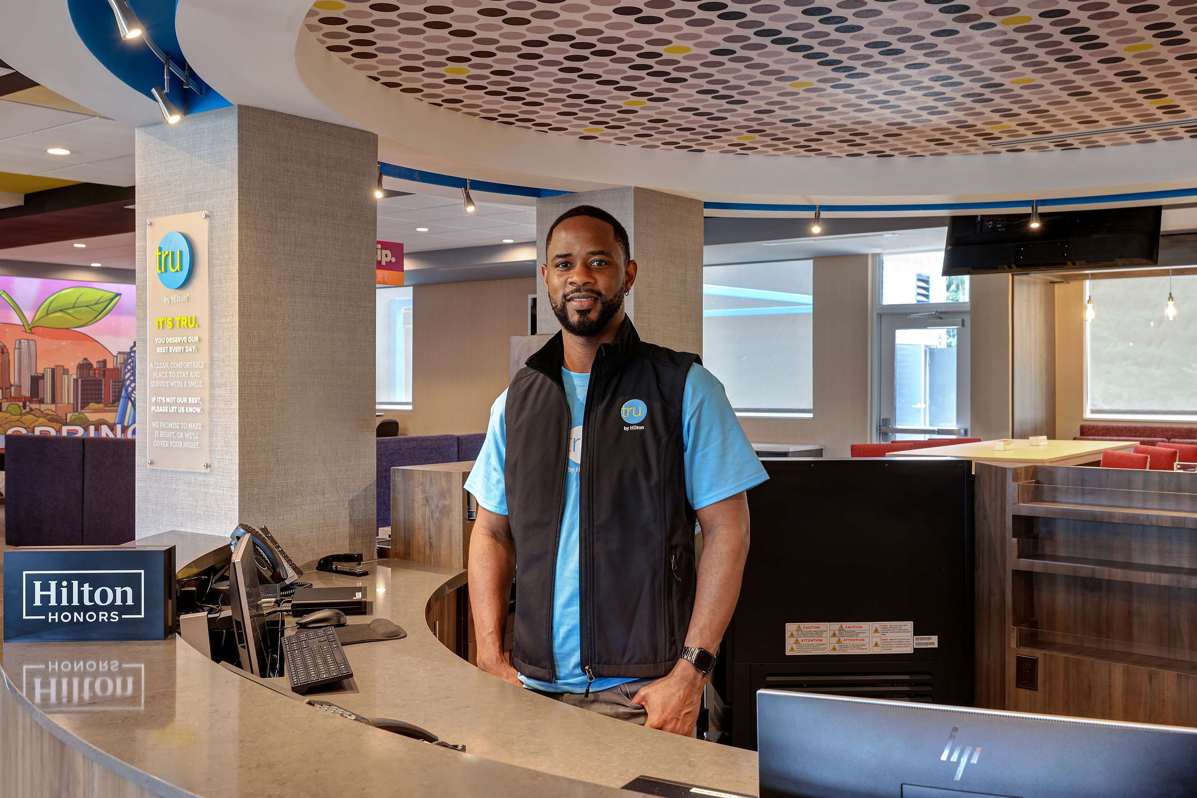 A hotel reception desk with a modern design, a digital screen, and a sign for Hilton Honors.