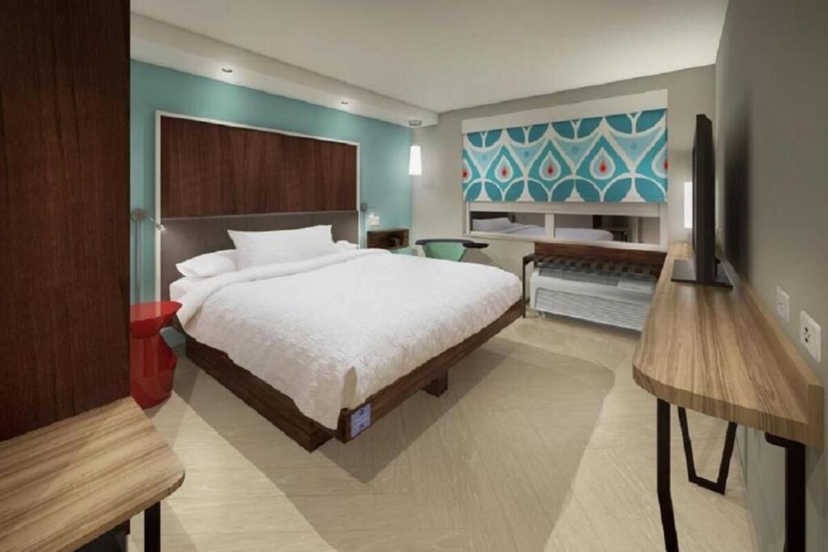 A modern hotel room with a large bed, a desk, a TV, and a patterned wall.