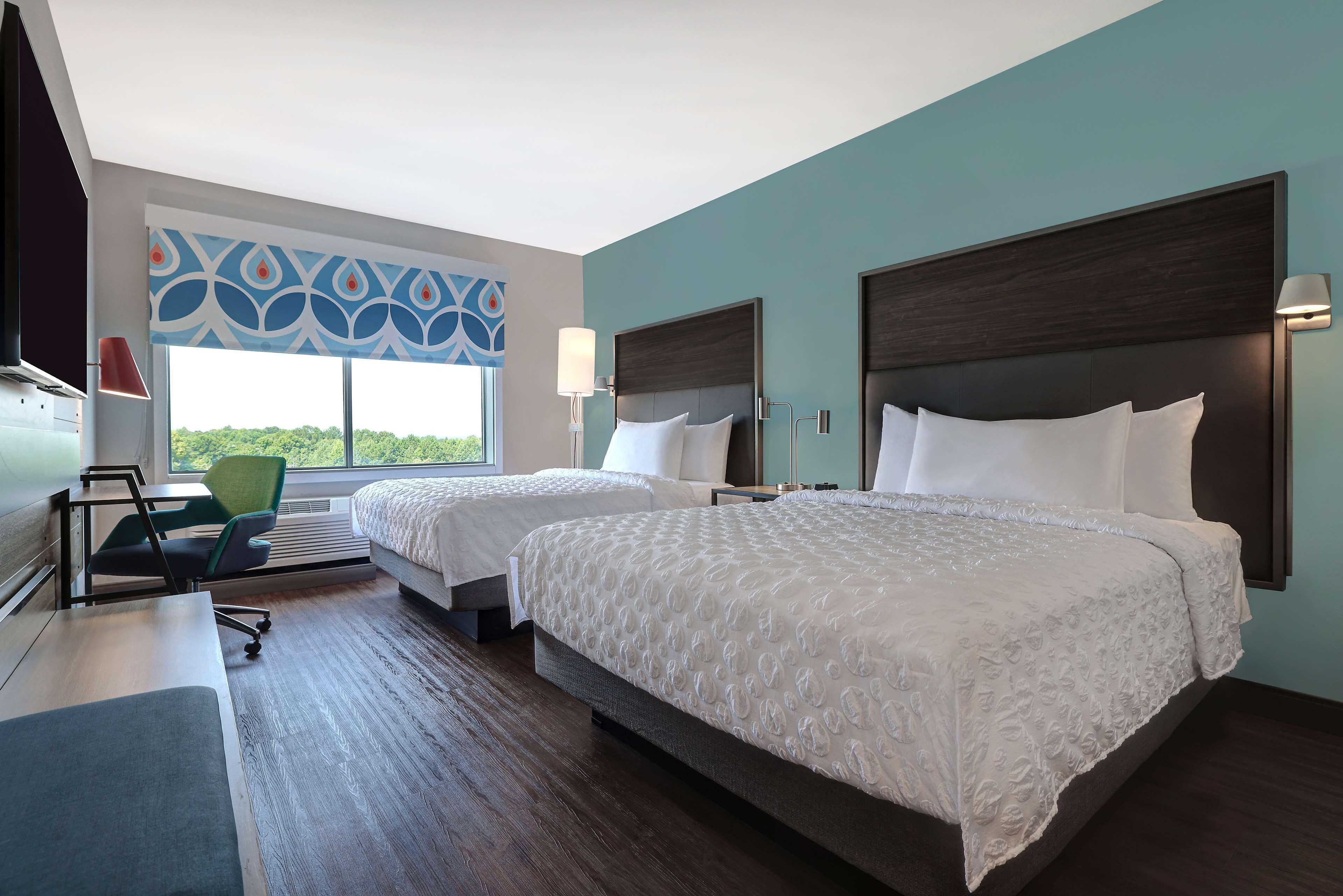 A hotel room with two beds, a desk, a chair, and a large window with a view.