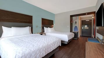 Habitación de hotel con dos camas, un escritorio, un televisor y una puerta que da al baño.