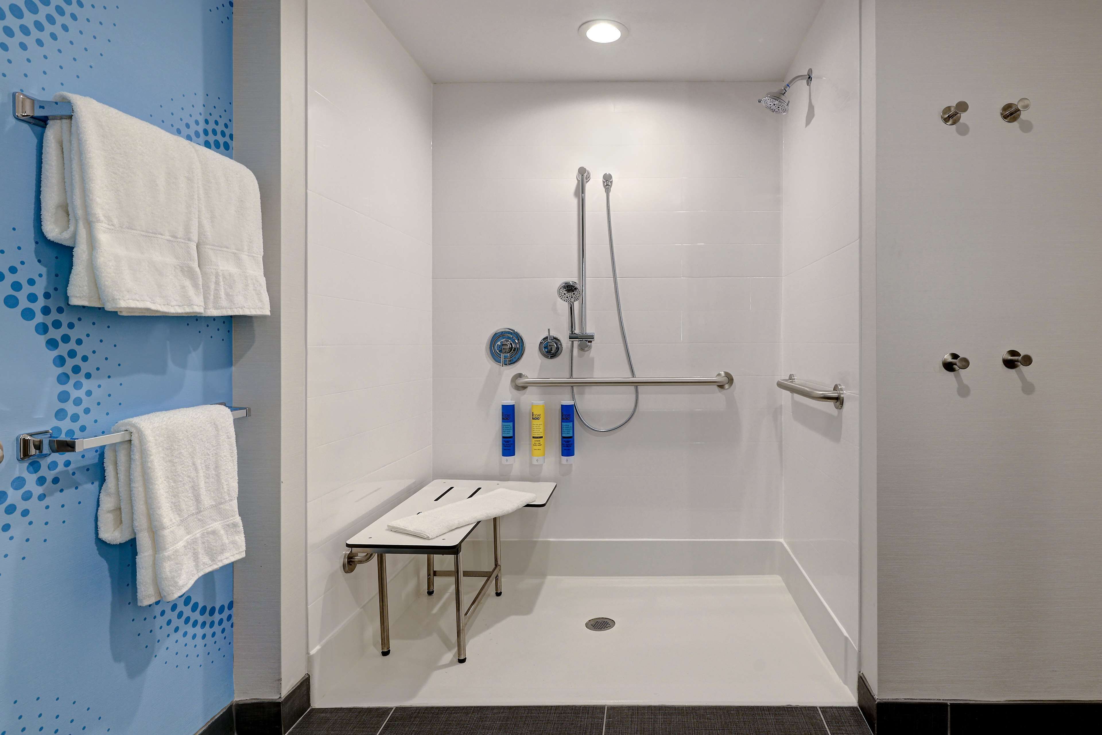 Un bagno moderno con doccia, maniglie di sostegno, porta asciugamani e un tavolino.