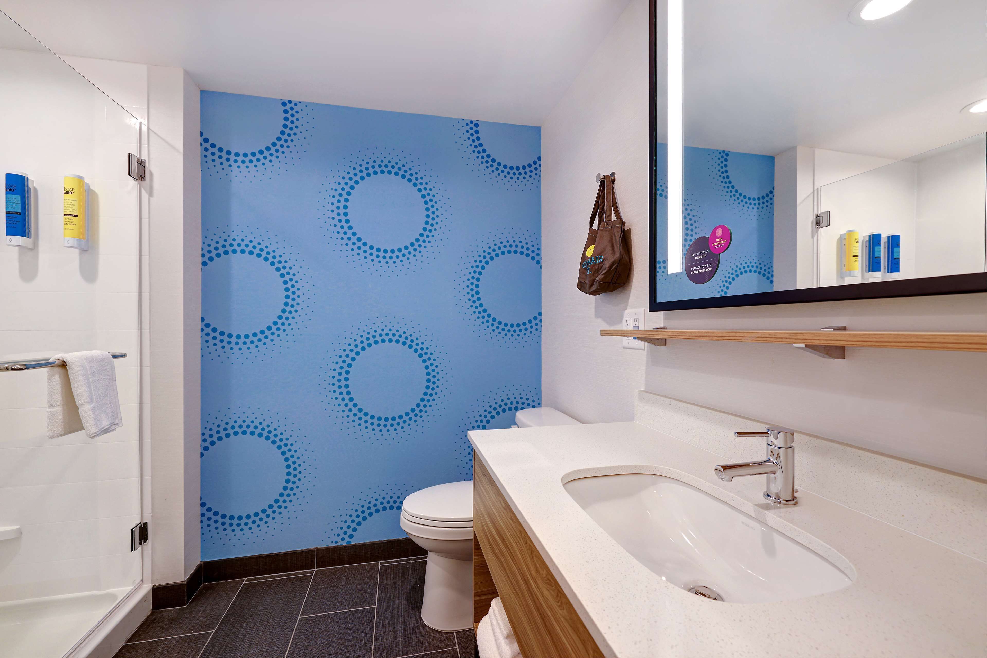 Ein Badezimmer mit blauer Wandgestaltung, einer weißen Toilette, einem Waschbecken mit Holzschrank und Pflegeprodukten an der Wand.