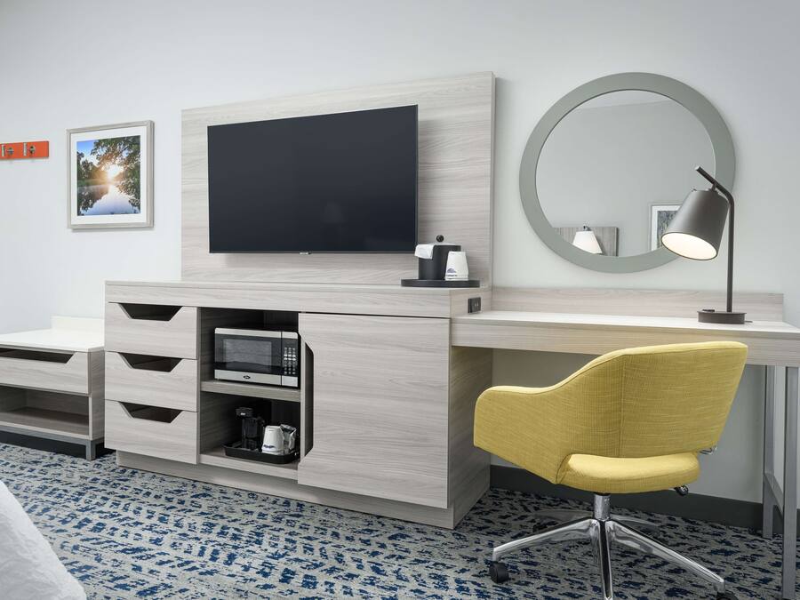 Hotellihuoneessa on suuri, litteänäyttöinen televisio, työpöytä tuolilla, kahvinkeitin ja mikroaaltouuni. Seinällä on kehystetty kuva ja työpöydän yläpuolella pyöreä peili.