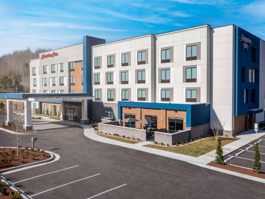A Hampton Inn hotel with a modern design, featuring a central courtyard with seating and a covered walkway.