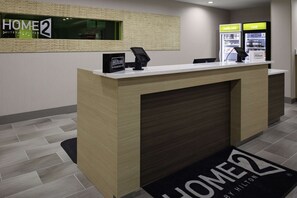 Ein moderner Hotelrezeptionstresen mit einem digitalen Telefon und einem Schild mit der Aufschrift 'HOME2 by Hilton' und 'Hilton Honors'.