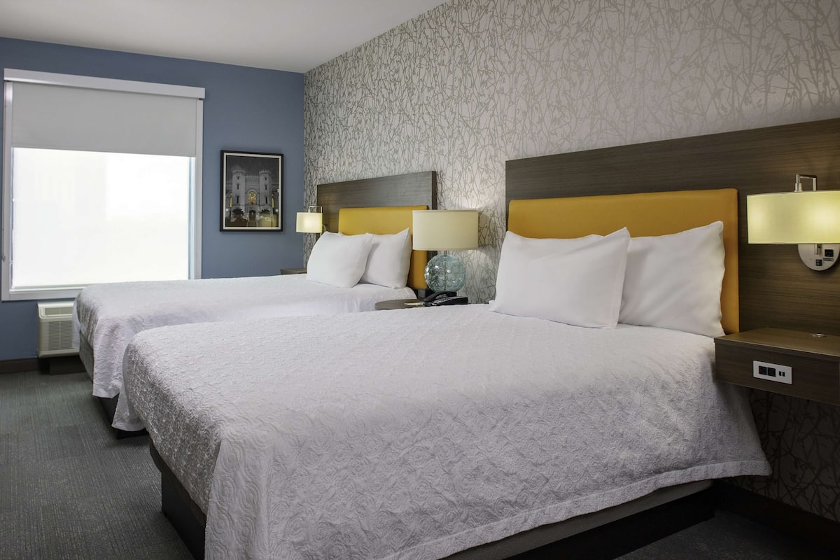 A hotel room with two beds, a large window, and a patterned wall.