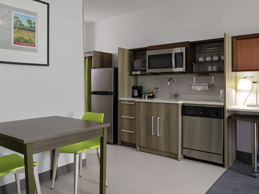 Une cuisine compacte équipée d’un réfrigérateur, d’un four à micro-ondes et d’un lave-vaisselle, ainsi qu’une table à manger avec des chaises et un tableau encadré au mur.