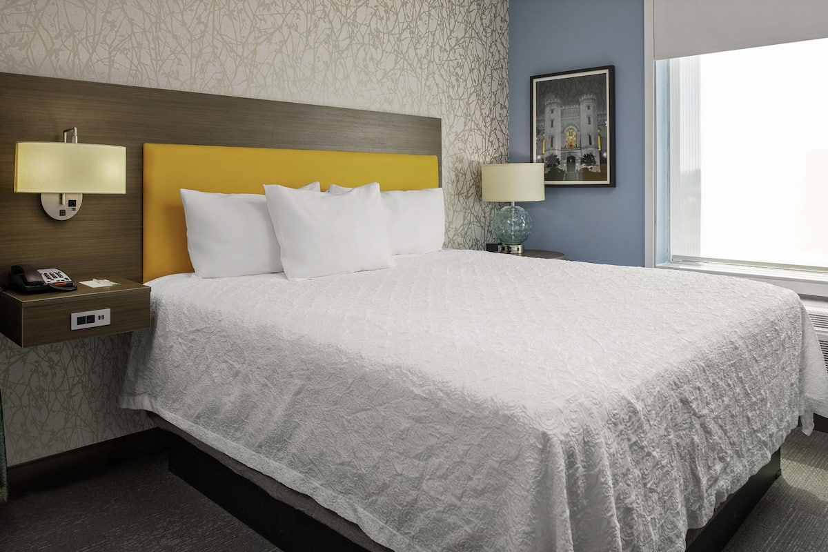A hotel room with a large bed, two bedside lamps, a nightstand with a phone, and a window with a view.