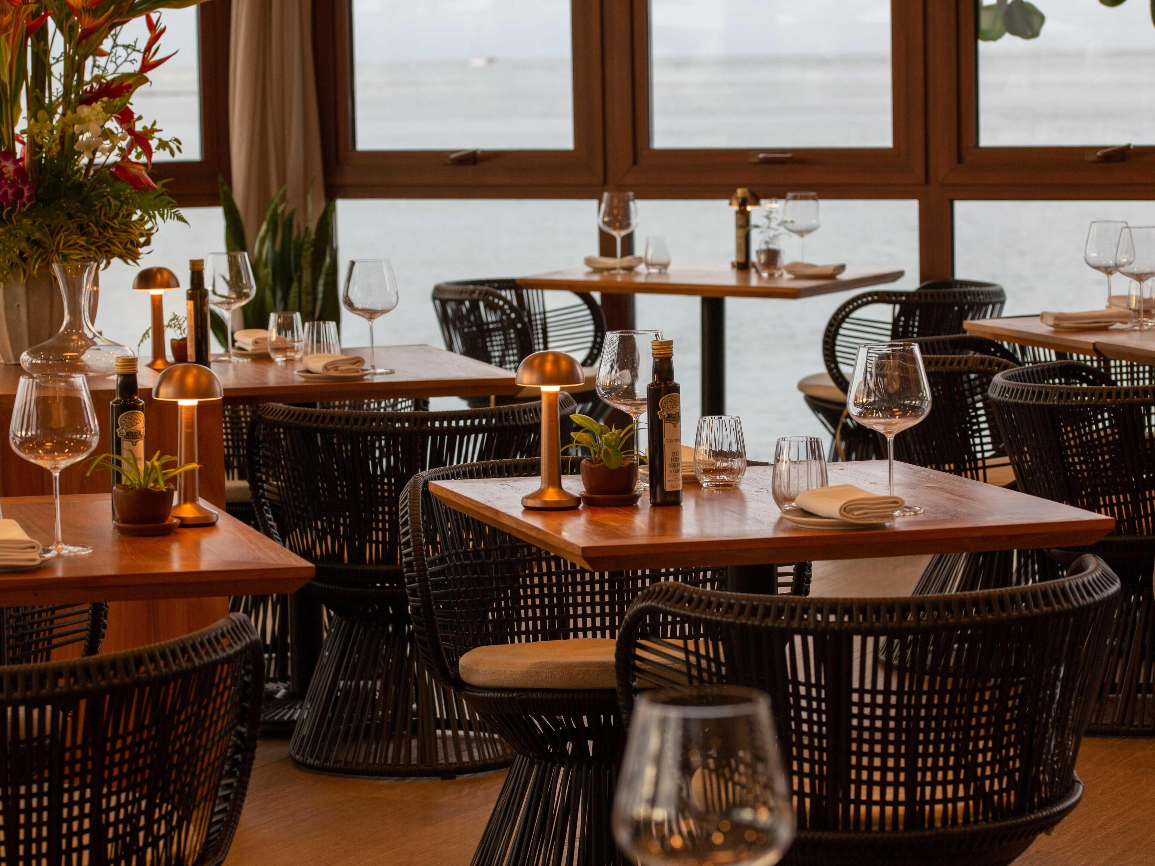 A restaurant with wicker chairs and tables, some with wine glasses and bottles.