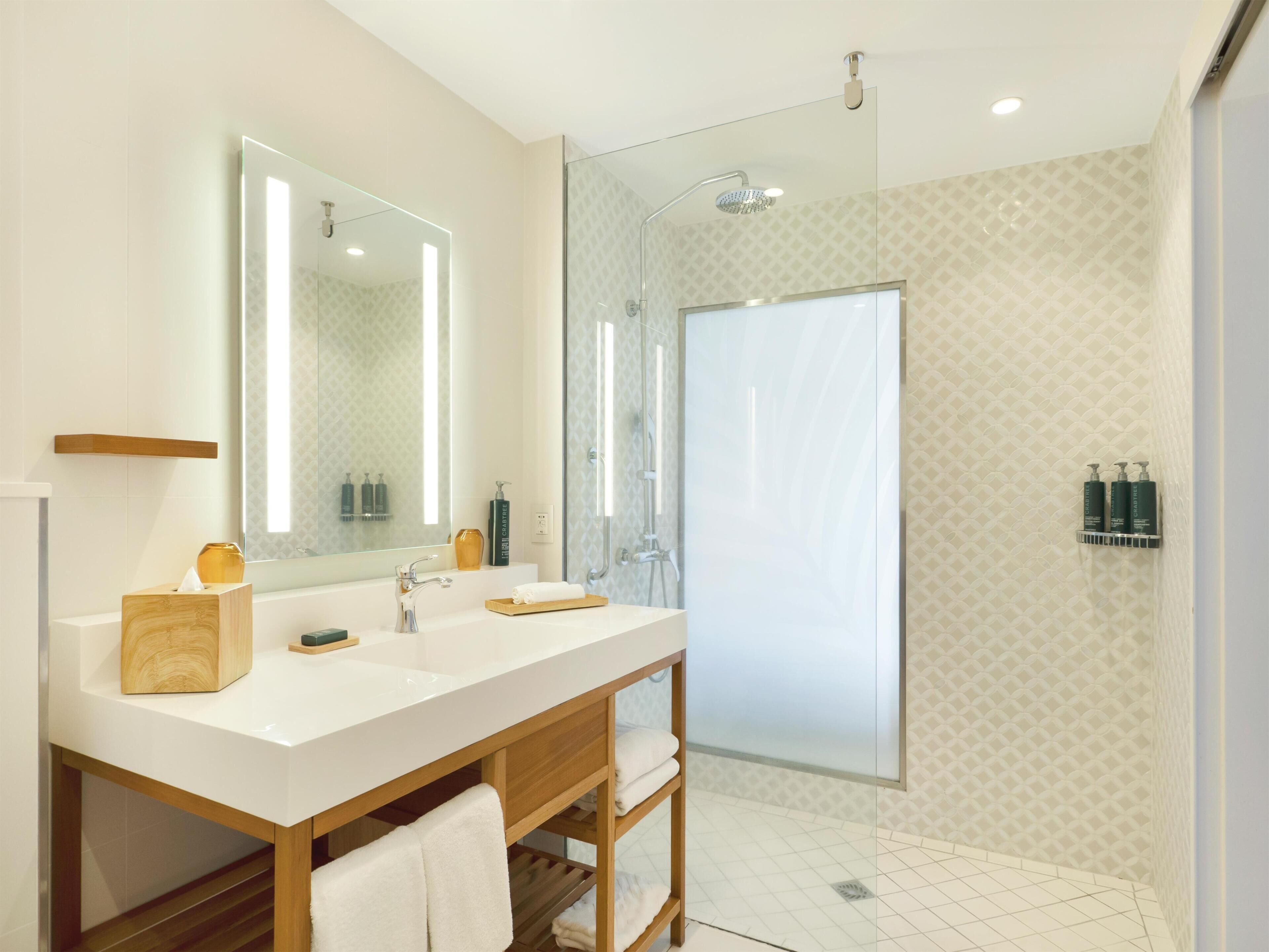 A modern bathroom with a large mirror, two sinks, a shower, and a towel rack.