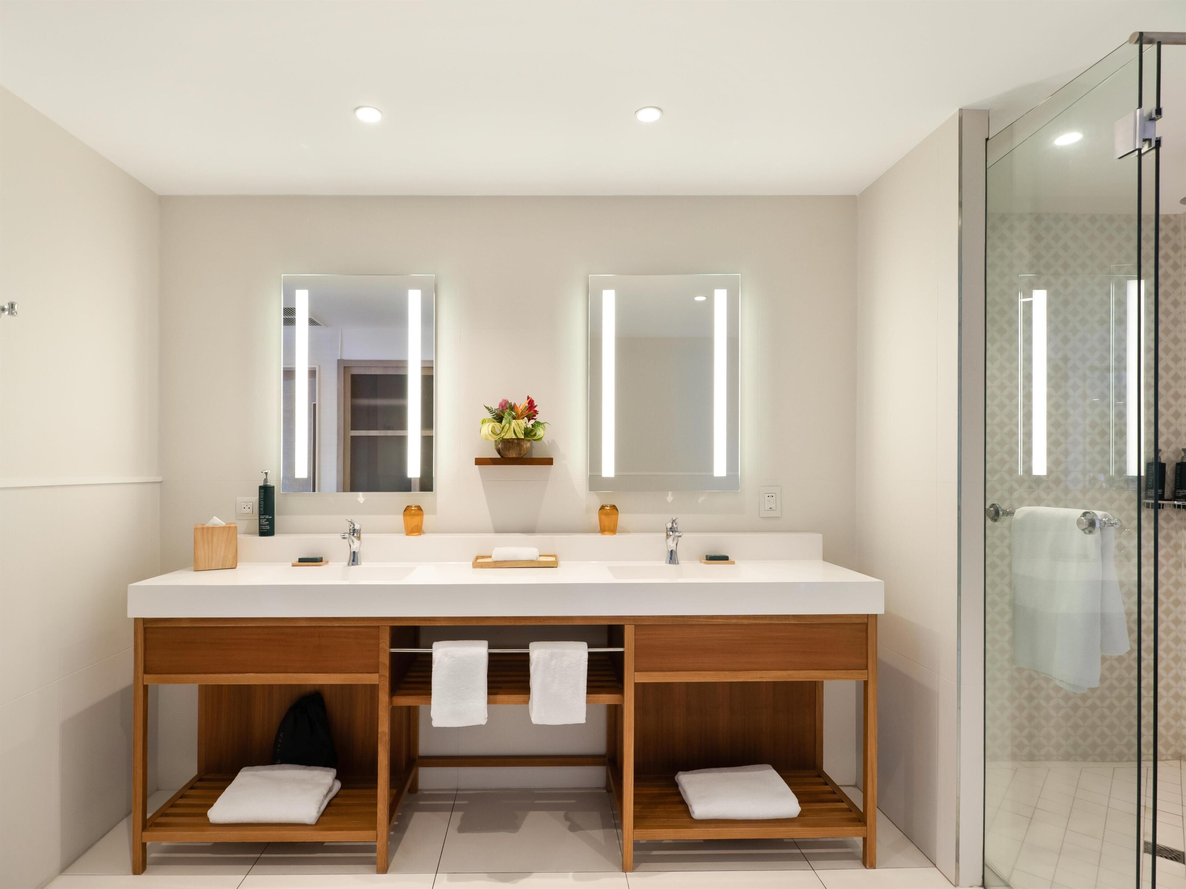A modern bathroom with a double sink, wooden vanity, and a glass shower enclosure.