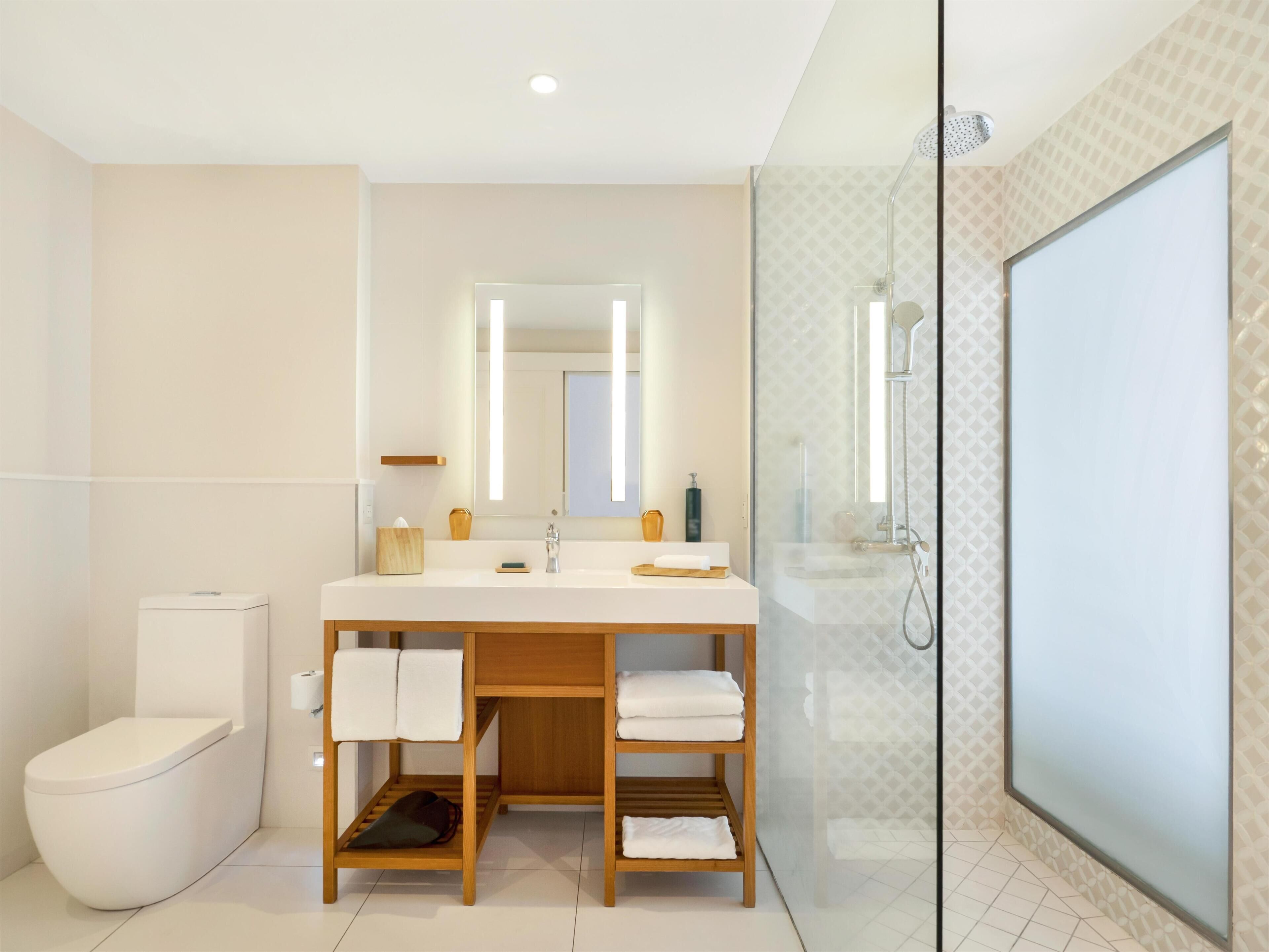 Un baño moderno con inodoro, lavamanos con espejo y ducha con mampara de vidrio.
