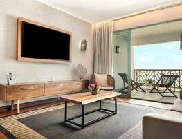 A modern living room with a flat-screen TV, wooden furniture, a bench, and a view of the sea.