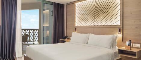 A modern hotel room with a large bed, a glass door leading to a balcony, and a wooden headboard with a geometric light design.
