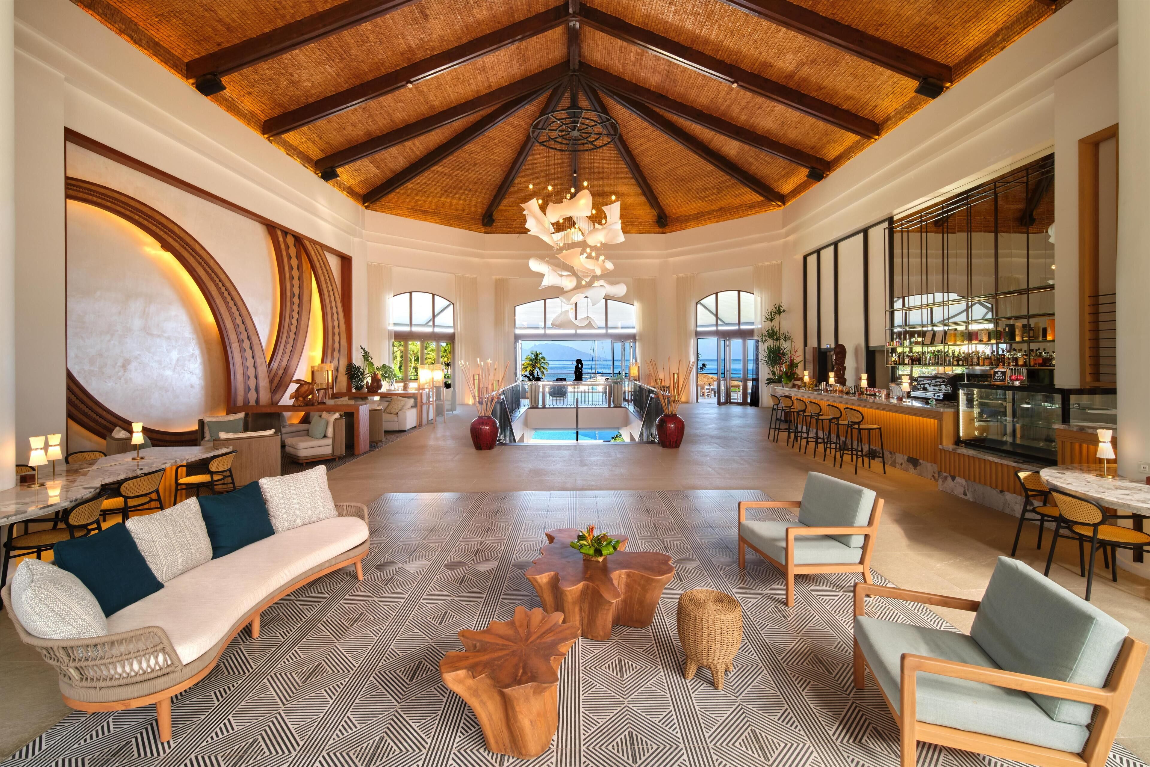 A spacious lobby with a high ceiling, a central seating area, and a bar with a view of the ocean.