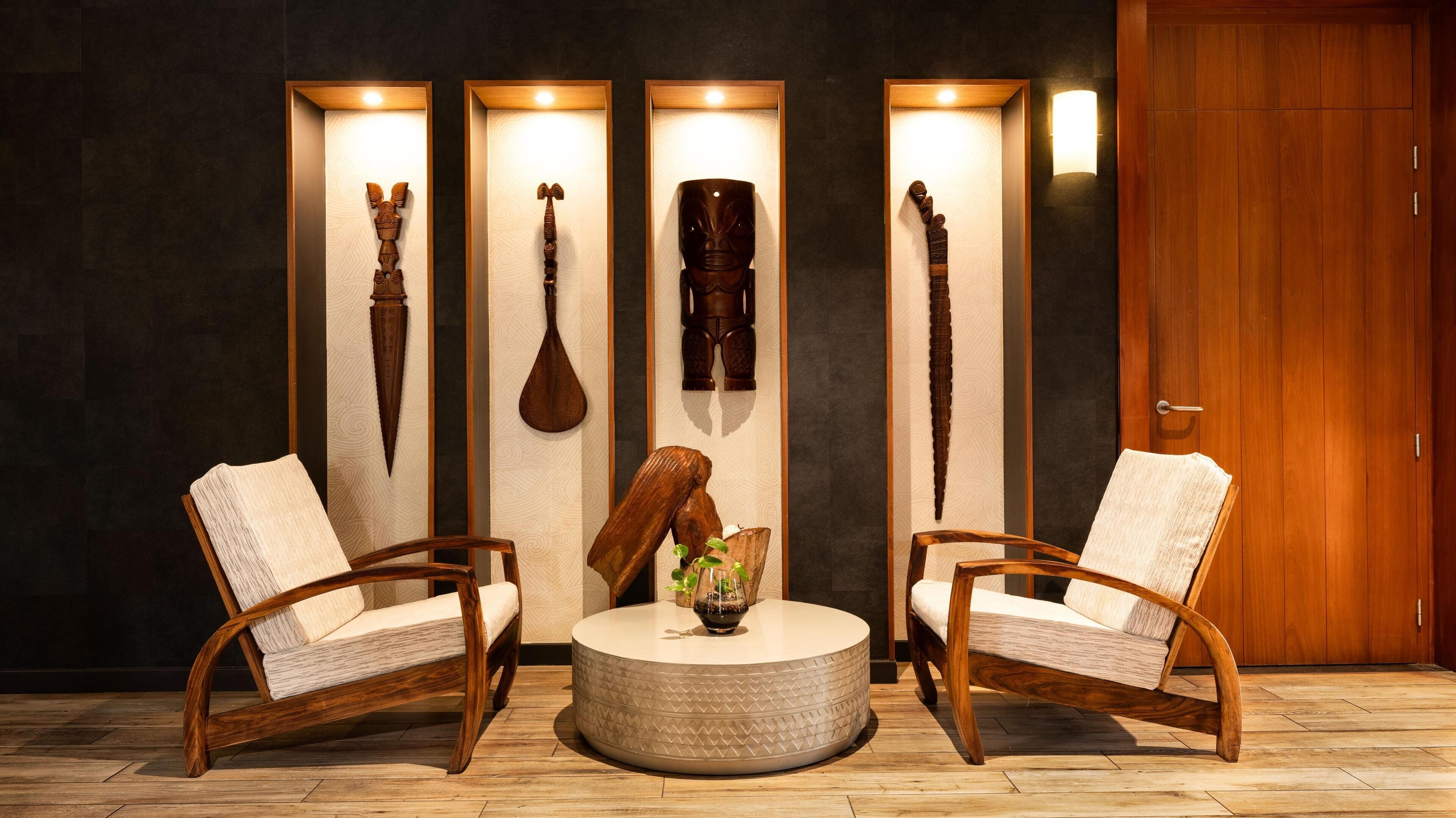 A room with two wooden chairs, a round table, and three wooden sculptures on the wall.