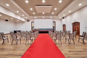 A conference room with a red carpet, rows of chairs, a large screen, and wooden doors.