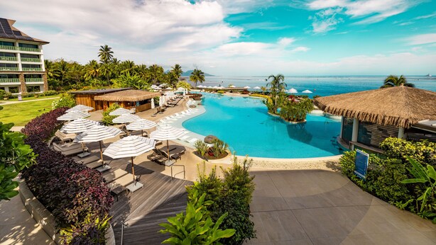 A resort with a large swimming pool, lounge areas with umbrellas, and a view of the ocean.