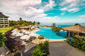 A resort with a large swimming pool, lounge areas with umbrellas, and a view of the ocean. - Hilton Hotel Tahiti (Faaa)