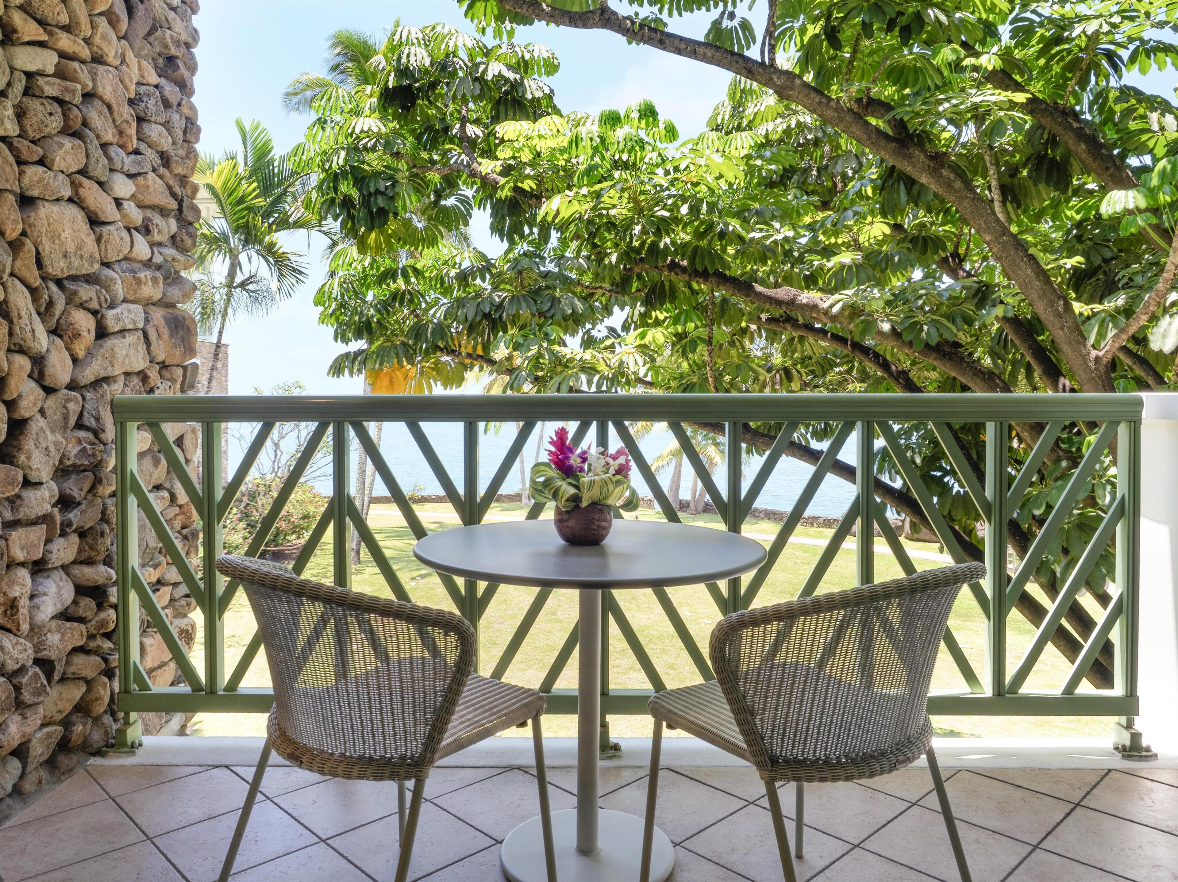 A balcony with two wicker chairs, a small round table with a flower vase, and a view of the sea.