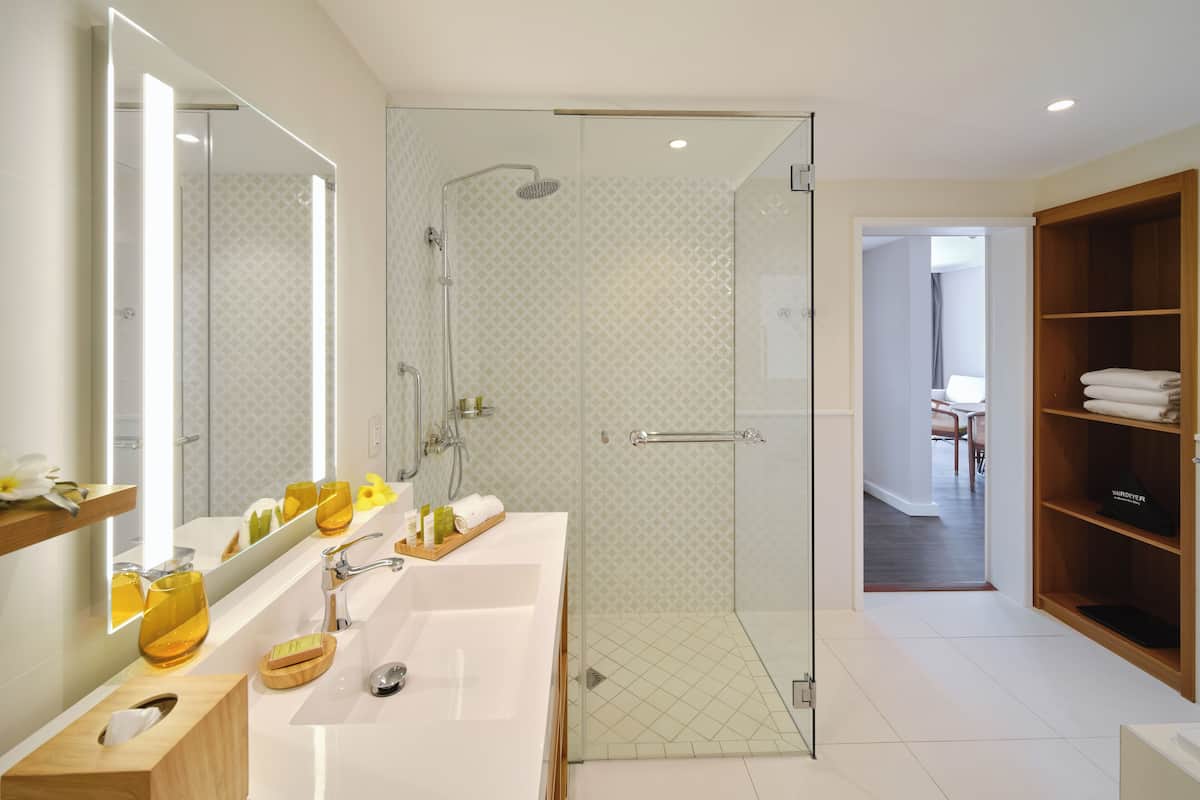 A modern bathroom with a glass-enclosed shower, a large mirror, and a vanity with toiletries.